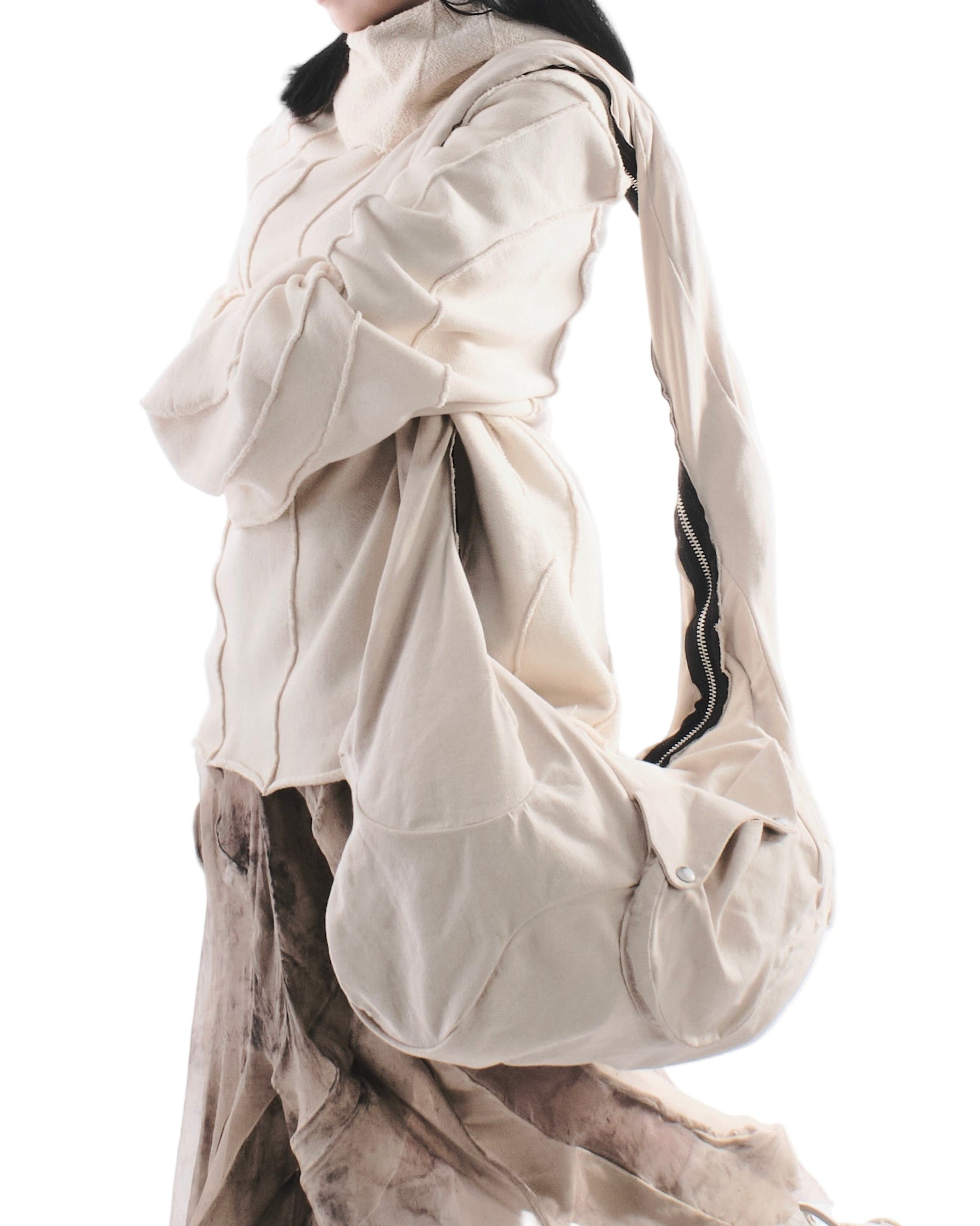 Person wearing a large beige bag over one shoulder on a white background