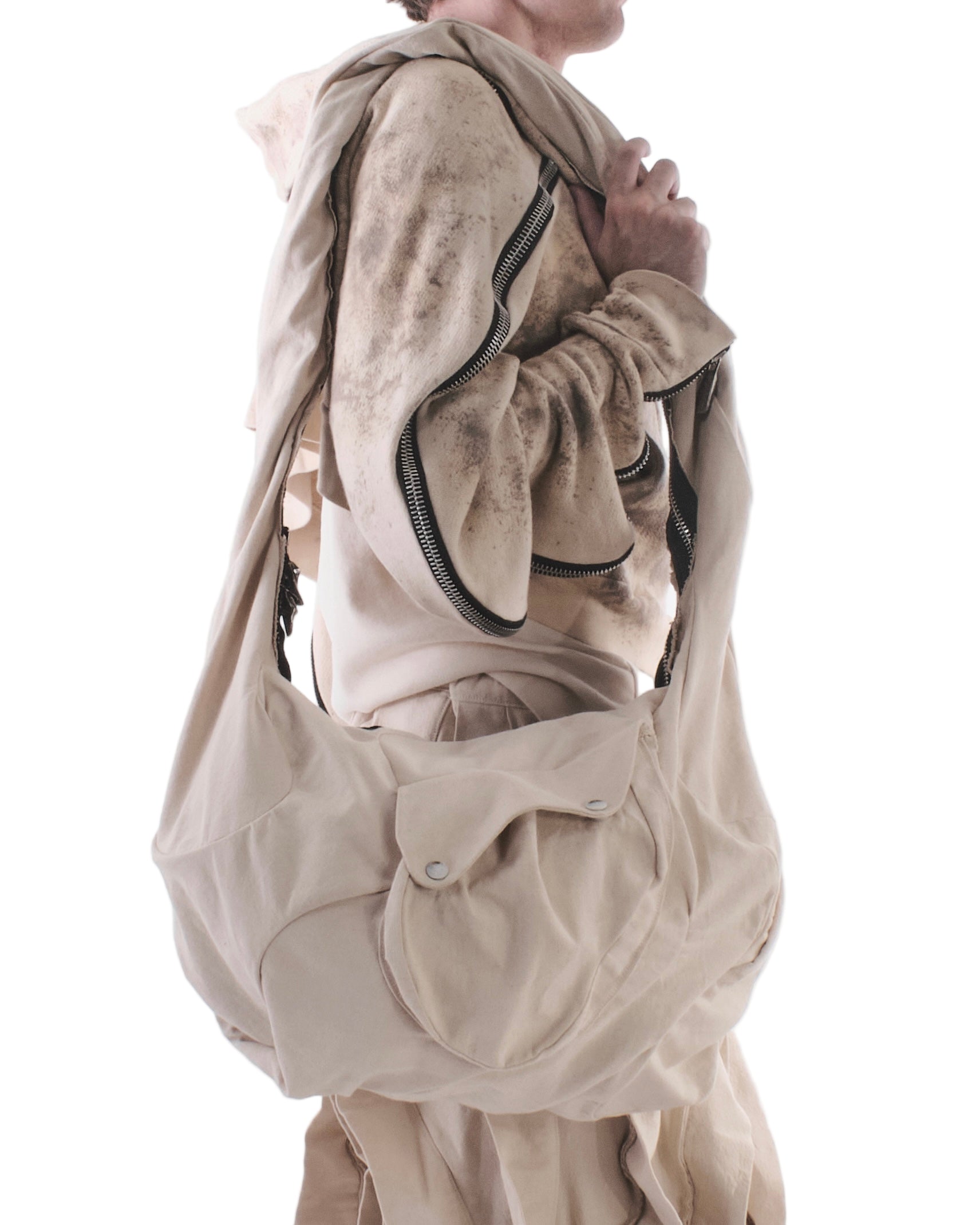 Person wearing a beige outfit with a matching bag on a white background