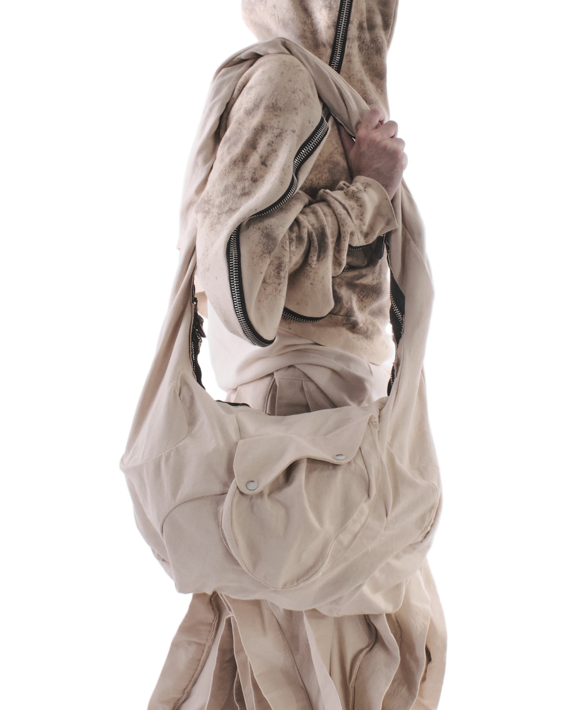 Person wearing a beige hoodie and pants with a matching bag on a white background