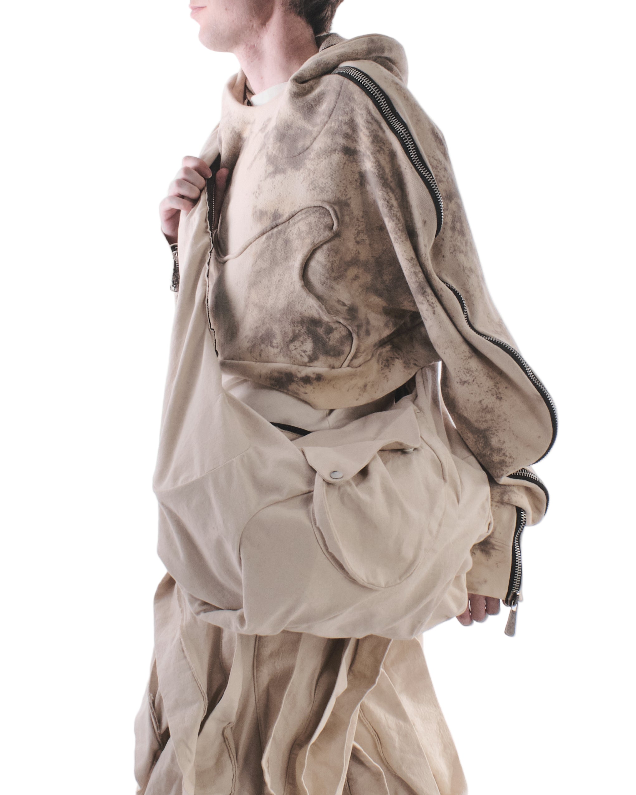 Person wearing a beige hoodie and pants with a matching bag on a white background